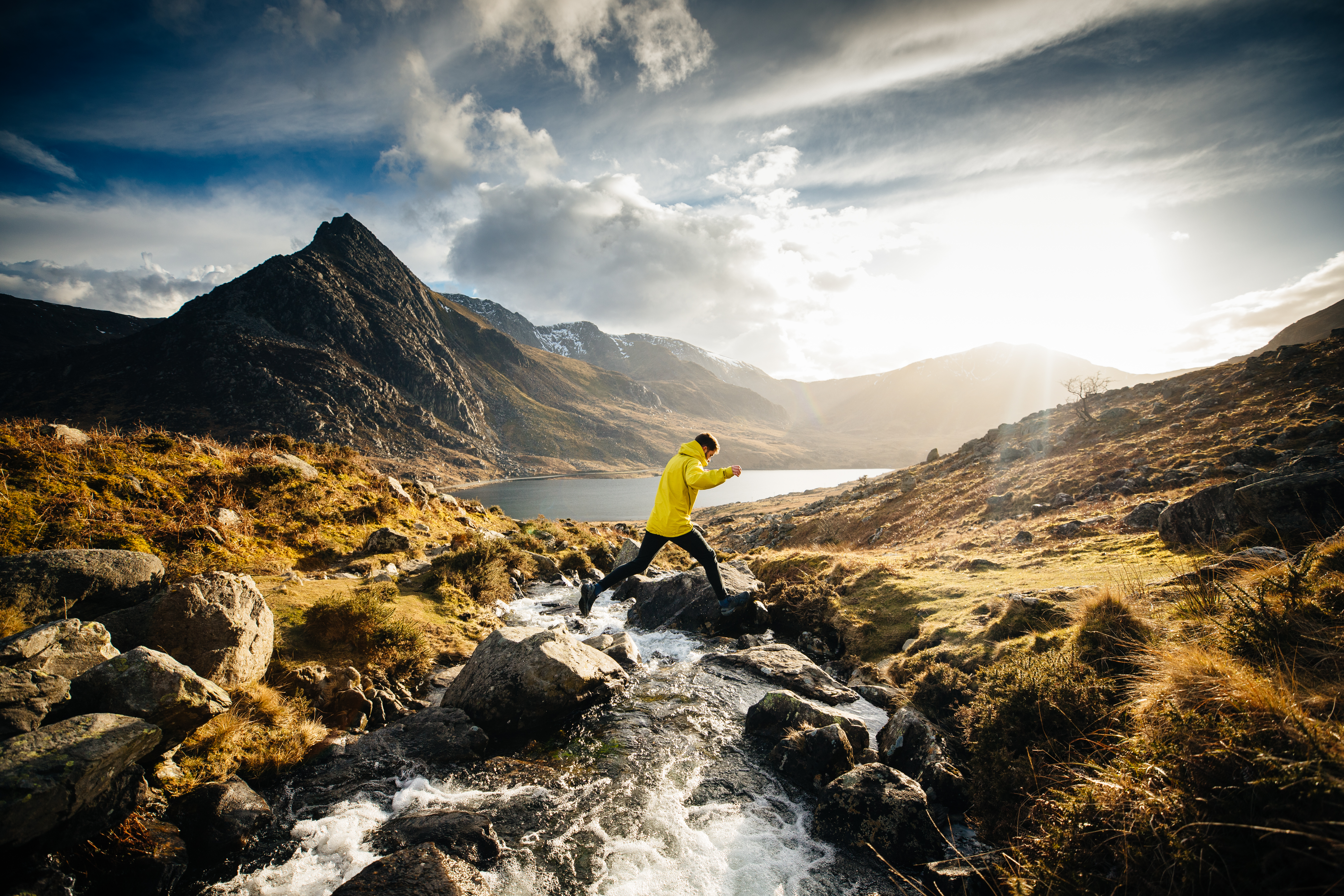 Man jumping from rock to rock across a stream flowing into a lake
