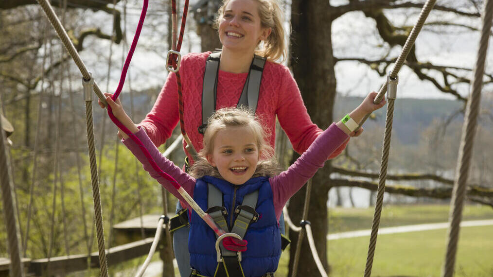 Femme et enfant portant des harnais de sécurité, sur un pont suspendu dans les arbres