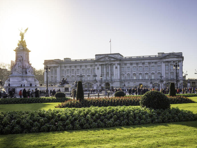 Blick auf den Buckingham Palace mit Gärten im Vordergrund und vorbeigehenden Menschen