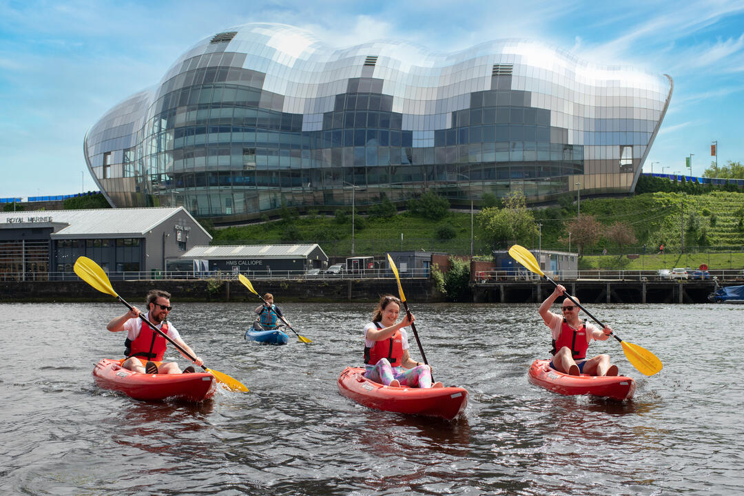 A group of people kayaking in front of an iconic building 