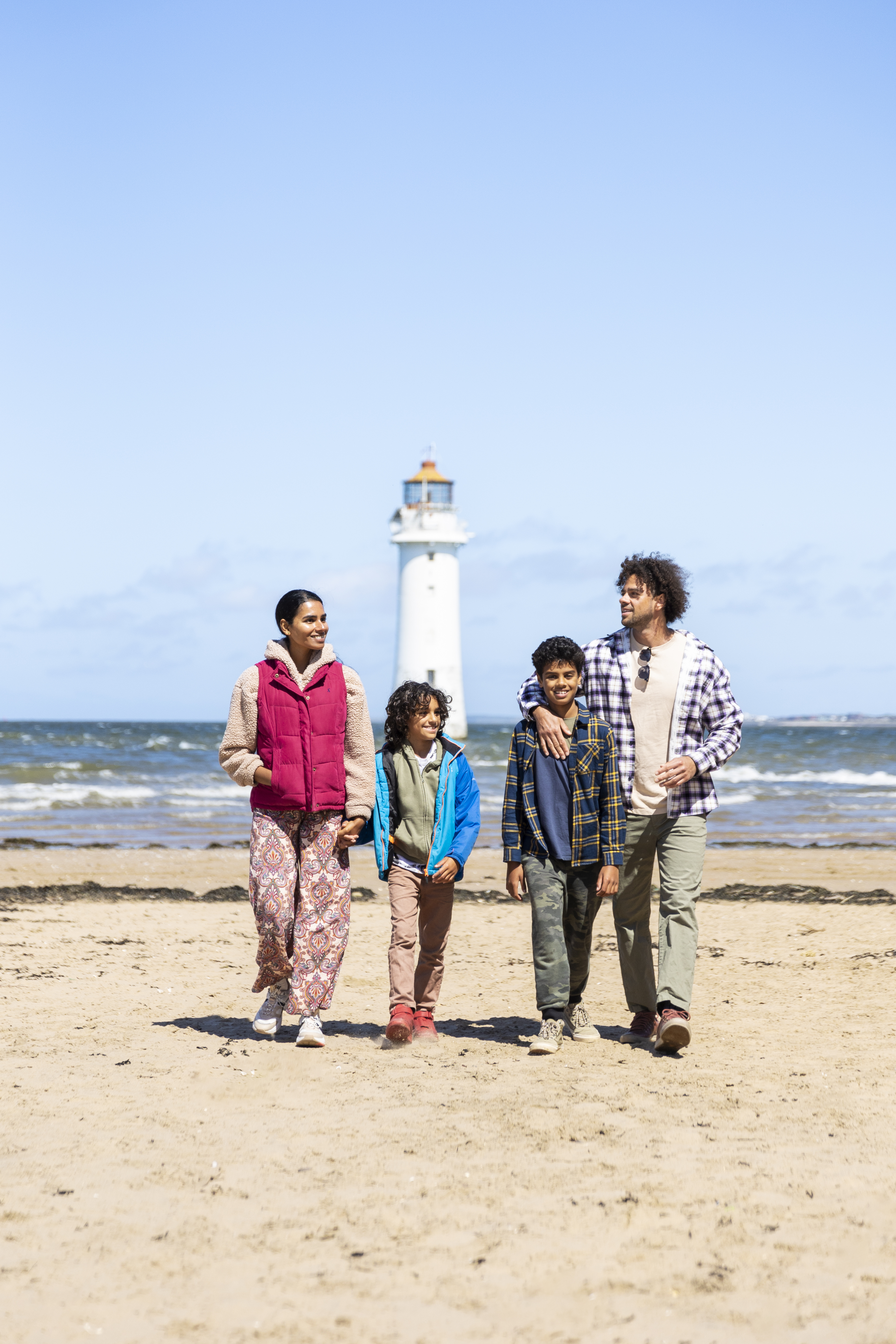 Family walk along a beach with a lighthouse in the background