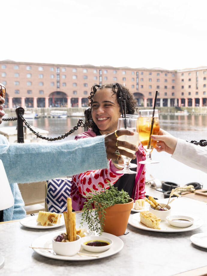 A group of friends raise a toast outside a restaurant with docks in the background