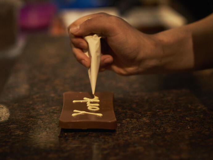 Person decorating dark chocolate with white chocolate piping
