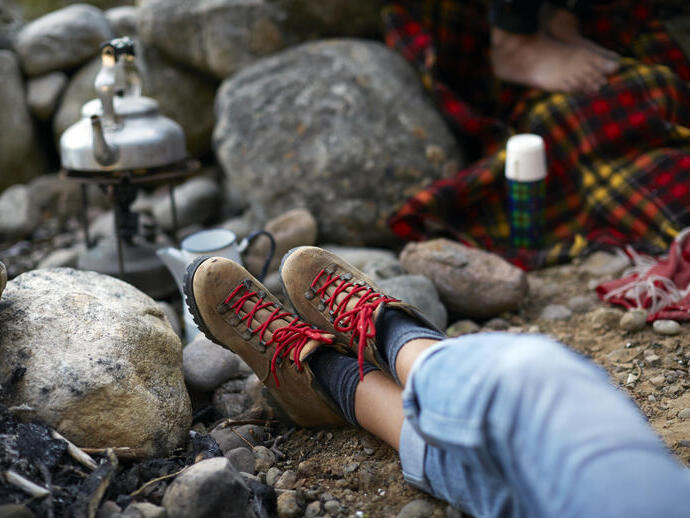 Woman sitting on a rocky ground, with legs outstretched waiting for a kettle to boil