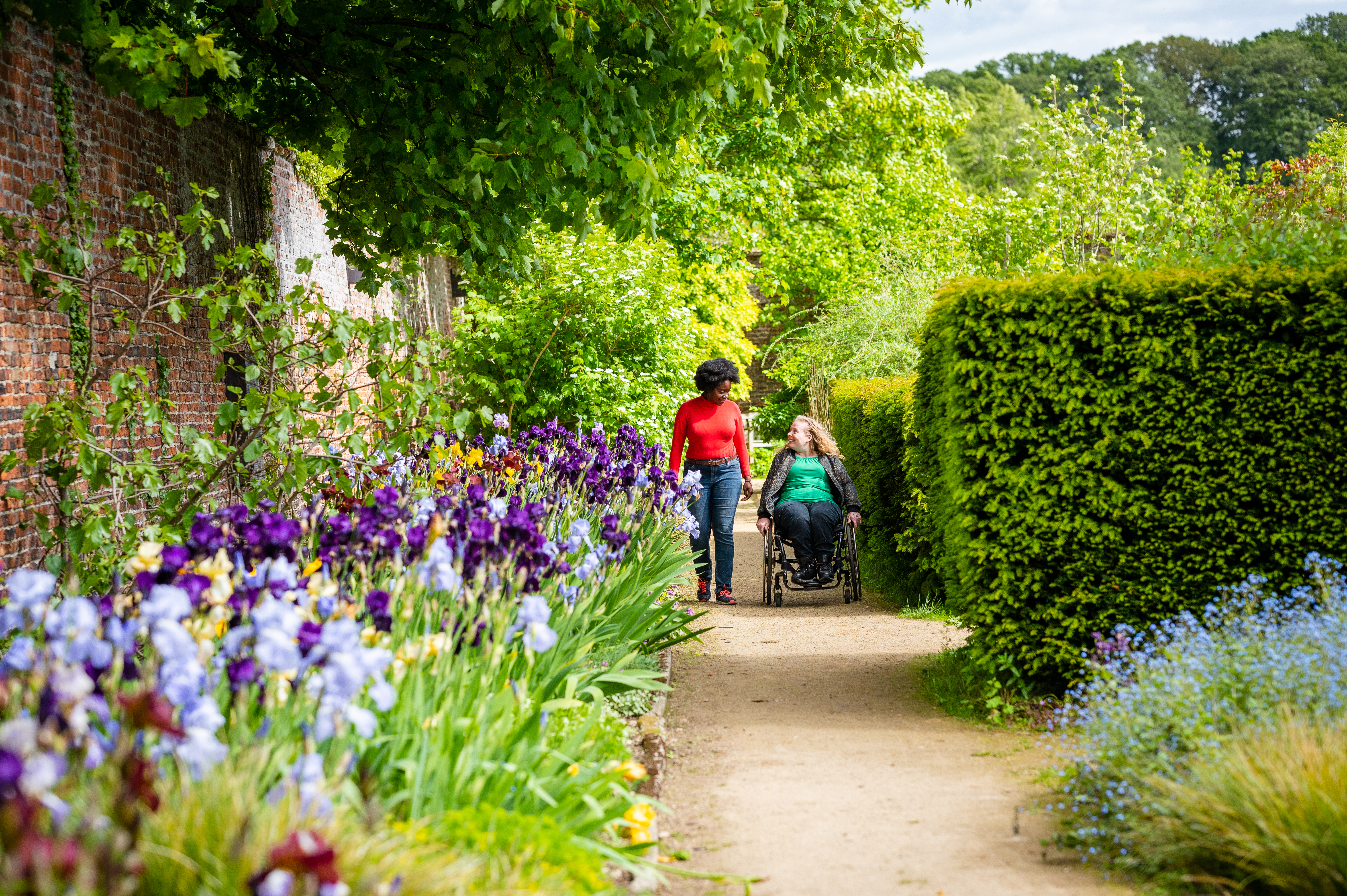 Two women walking, one using a wheelchair, meandering through a garden path.