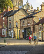 Two cyclists walking uphill with bikes in Lincoln, with Lincoln Castle in the background