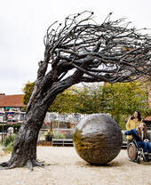 Dos mujeres, una en silla de ruedas, mirando una gran escultura de bronce en un jardín
