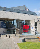 Exterior view of the Dundee Rep theatre with a person sitting outside on a bench.