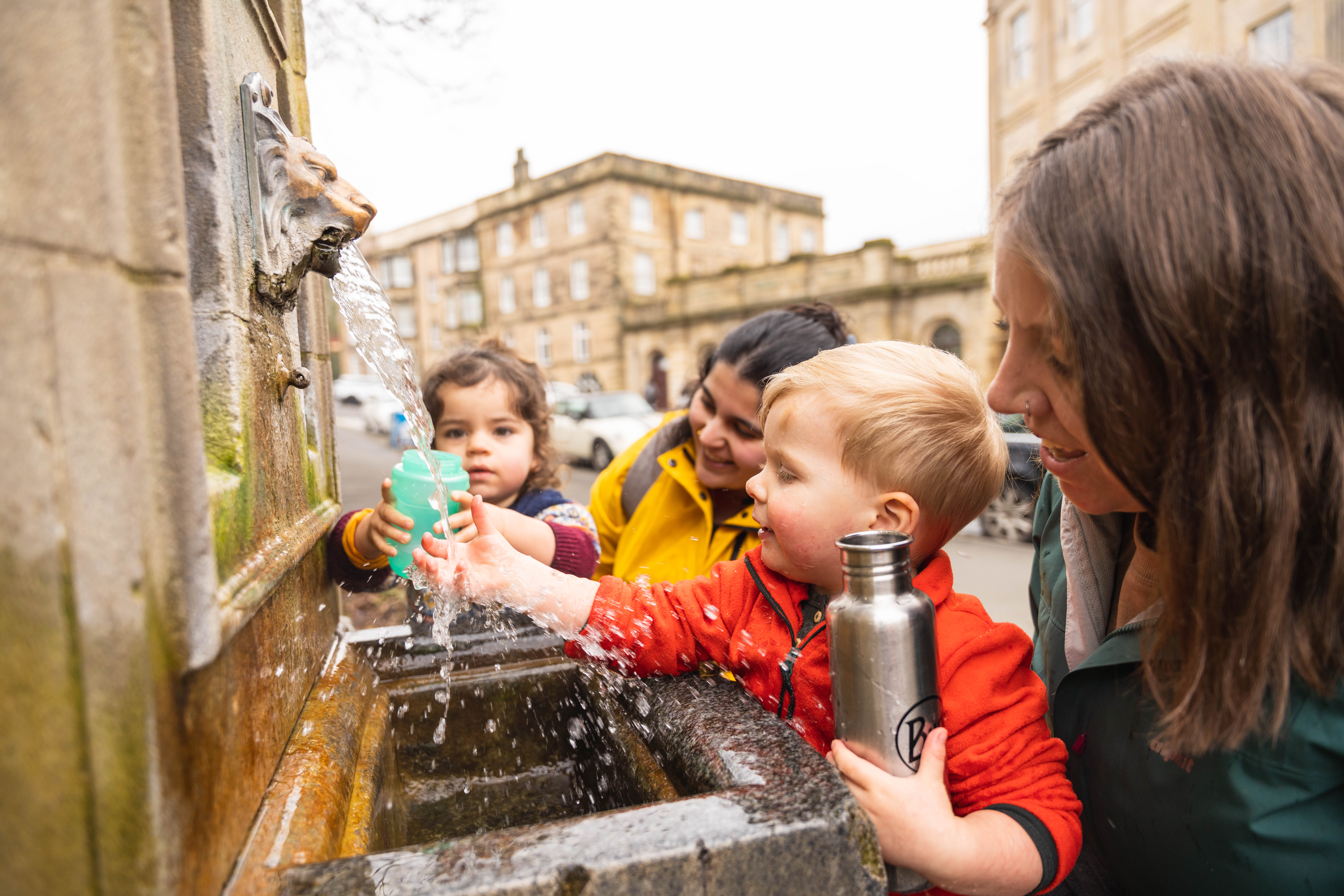 Two women and two small children getting water from a fountain