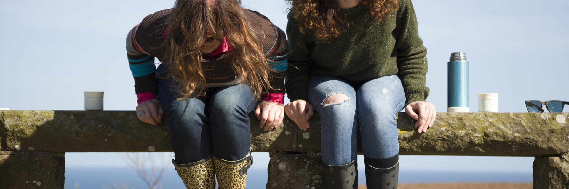 Dos mujeres sentadas en una valla de piedra, riendo
