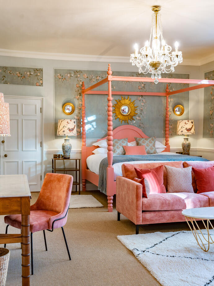 An interior shot of a colourful hotel room featuring a pink four poster bed