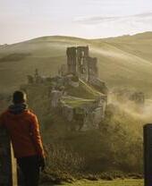 Man leaning on gatepost, looking at the ruins of a castle