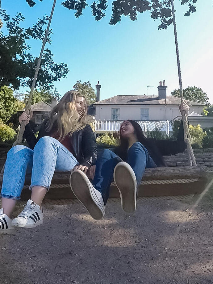 Two young women on swing in garden hanging from a tree