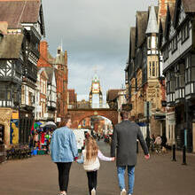 A family of three in front of the town clocktower in a shopping strip.