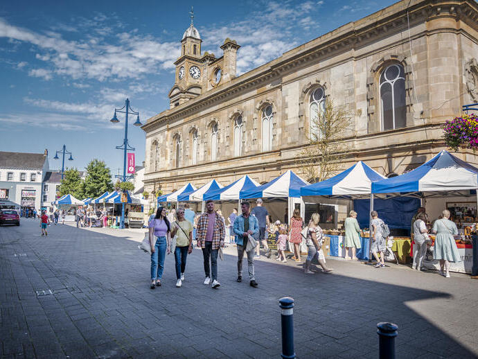 Group of friends walking in a town street past market stalls