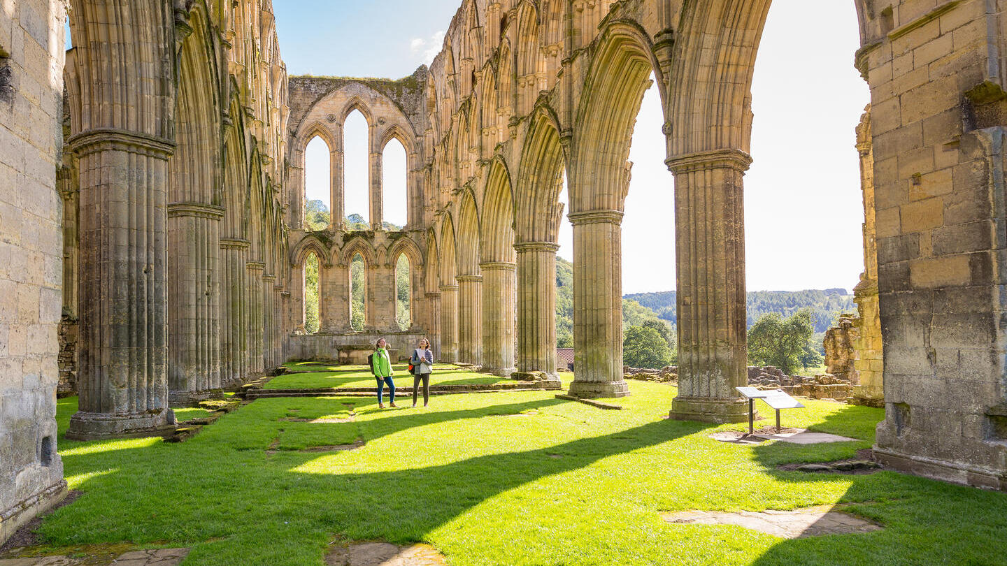 Due amiche nella navata centrale di un'abbazia in rovina sotto il sole.