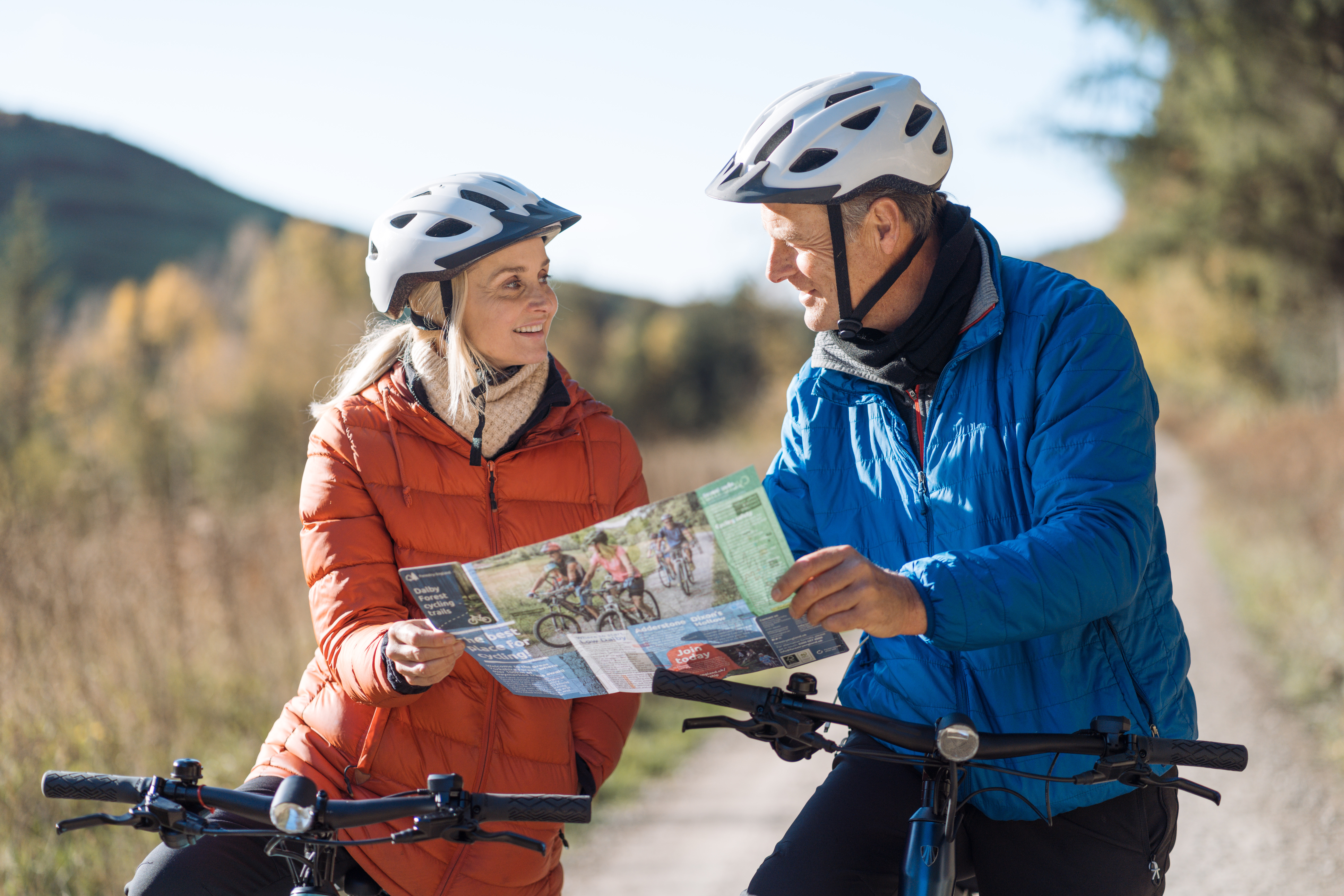A man and a woman look at a trail map while riding e-bikes through a forest bicycle forest path.
