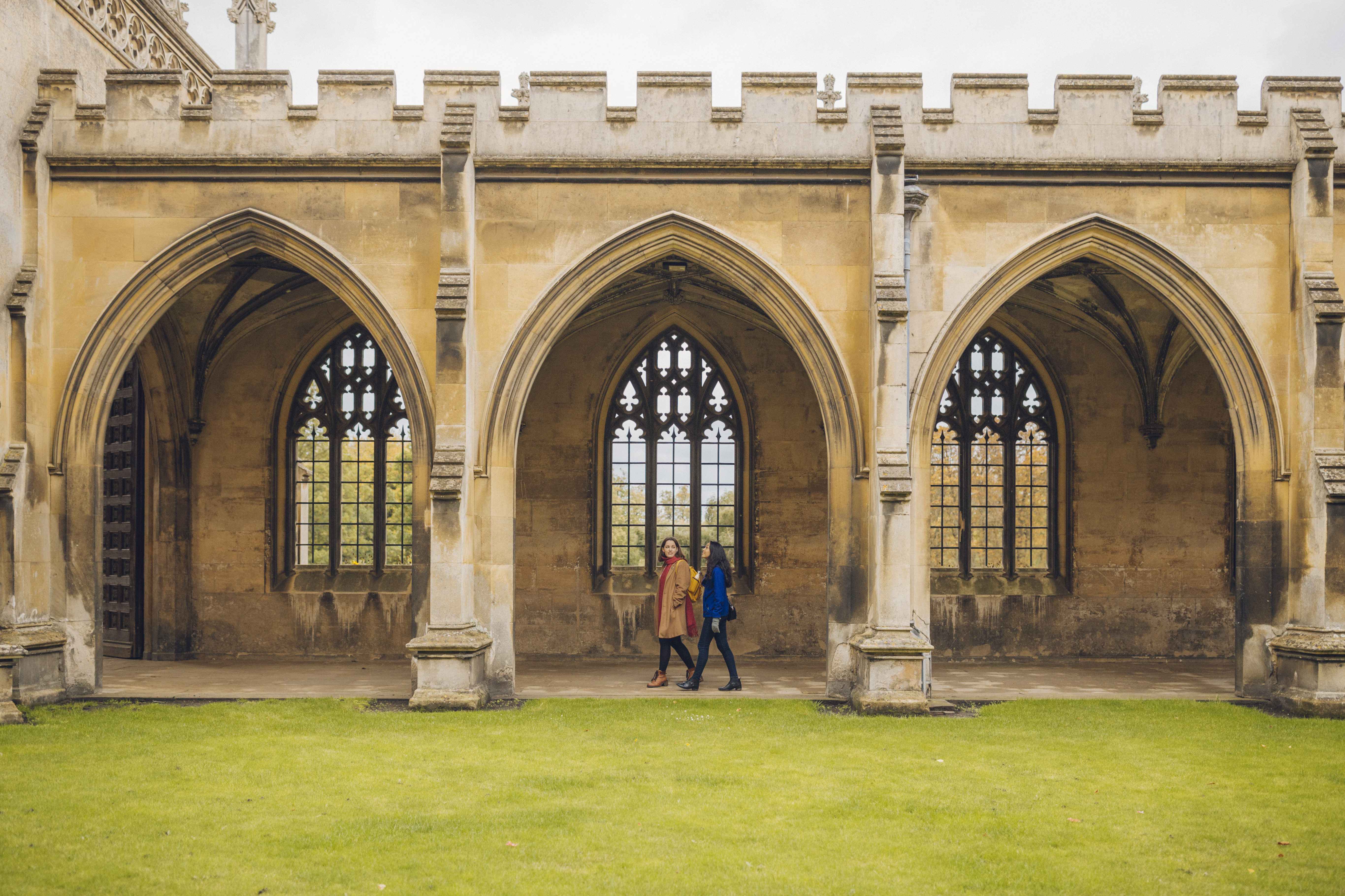Two women walking under the arches of a college quad