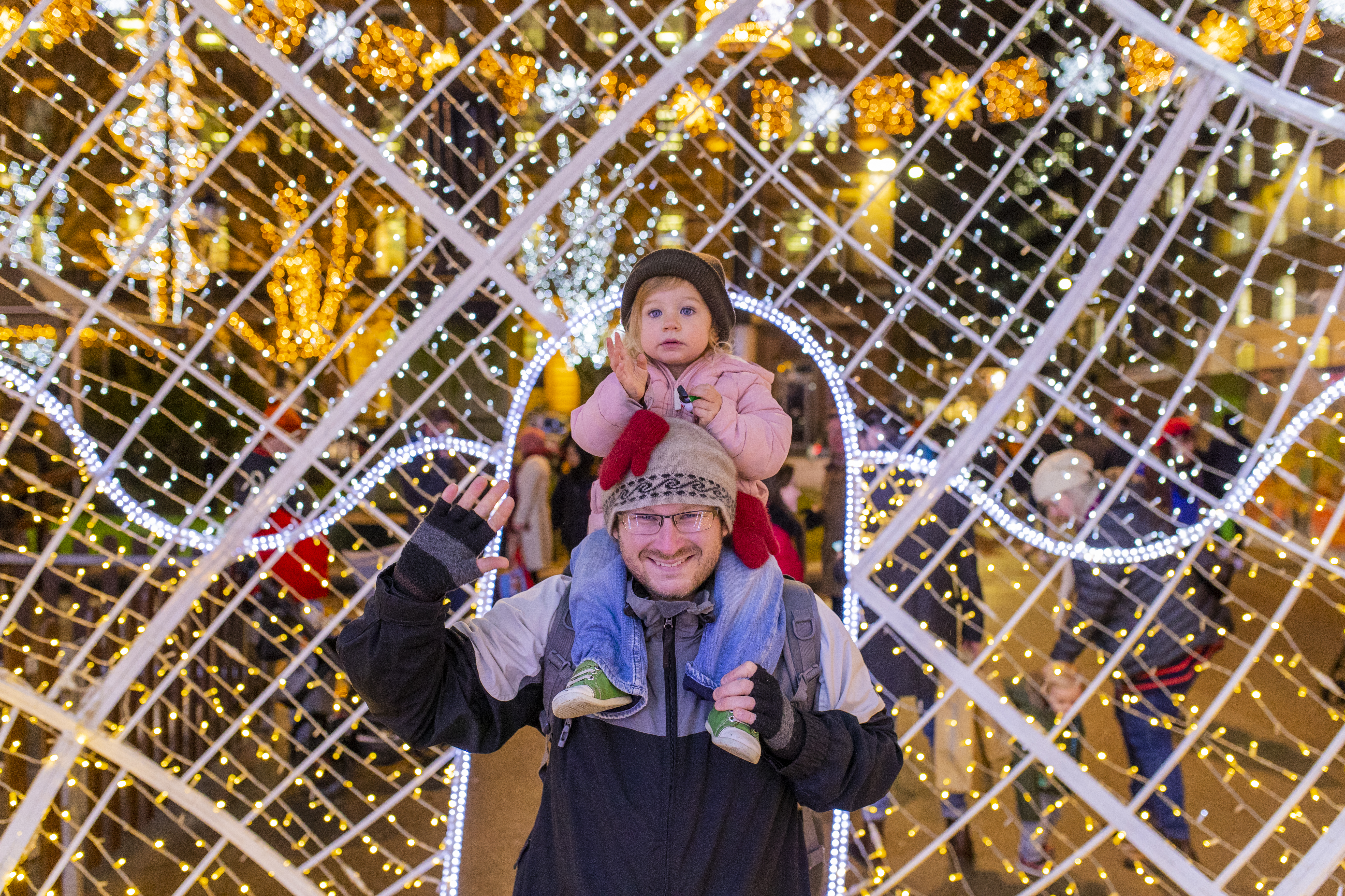 Un homme avec une petite fille sur les épaules devant des lumières