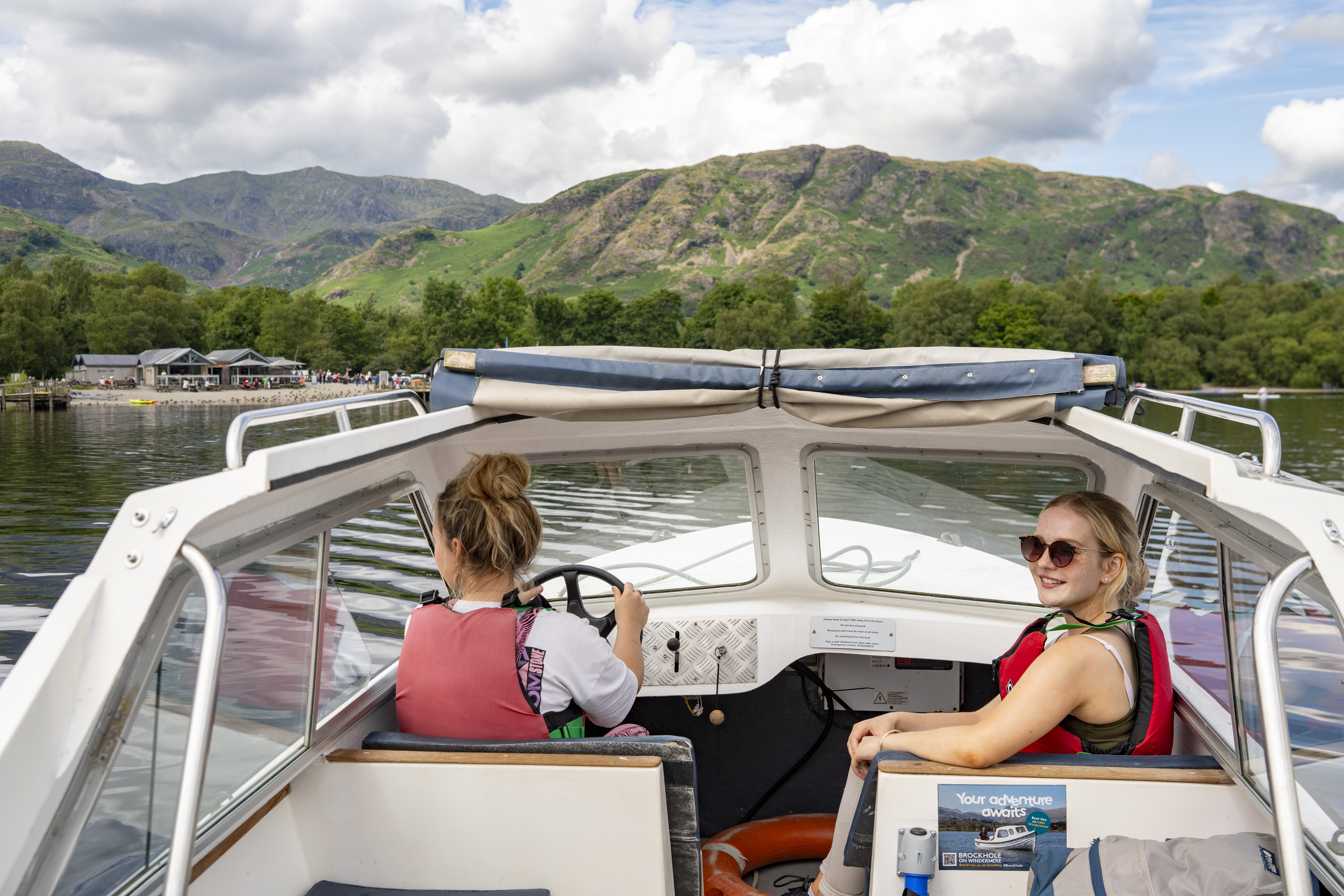 Town women sit ar the front of a boat on a lake with hills beyond