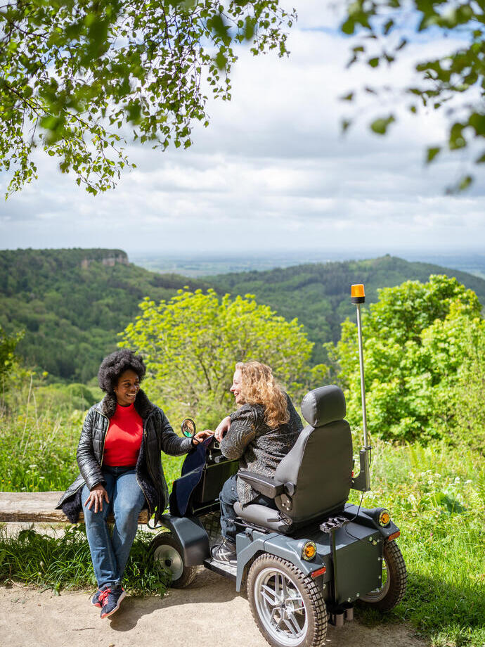 Two women on walking trail, one using a tramper, one sitting on a bench
