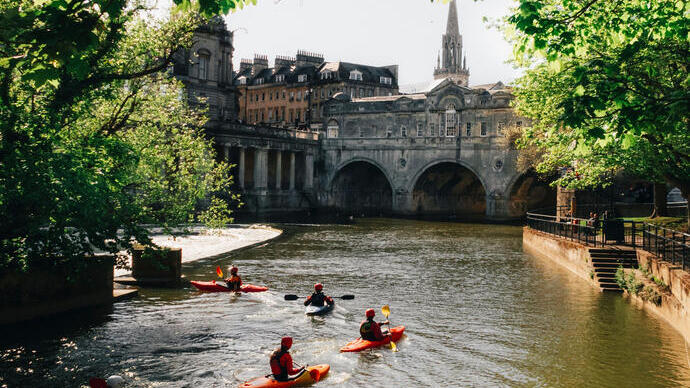 Group of people kayaking on the river by a bridge in a city