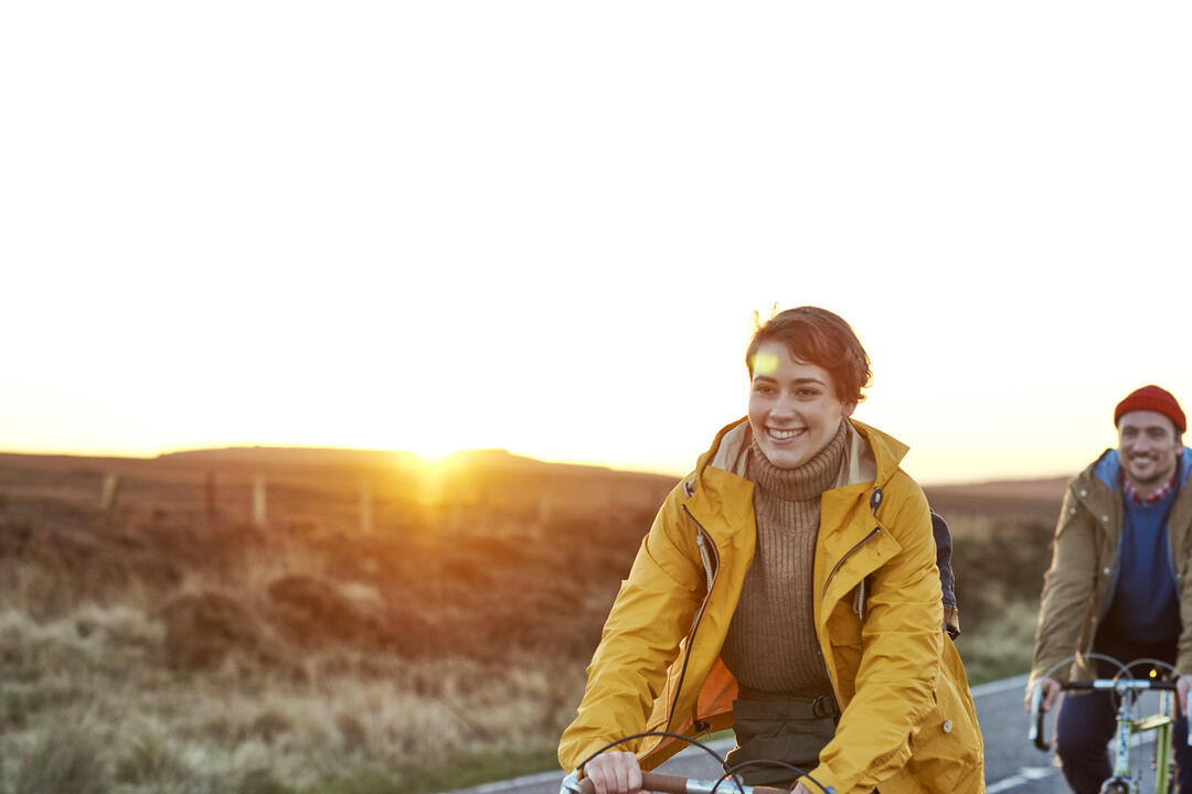 A man and woman cycling on the road near hilly countryside