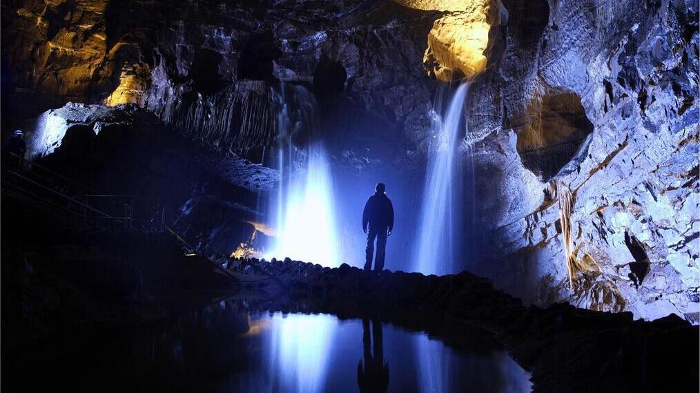 Hombre de pie junto a una cascada en una cueva oscura