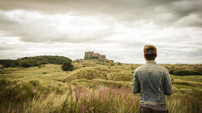 Man standing among dunes looking at a castle