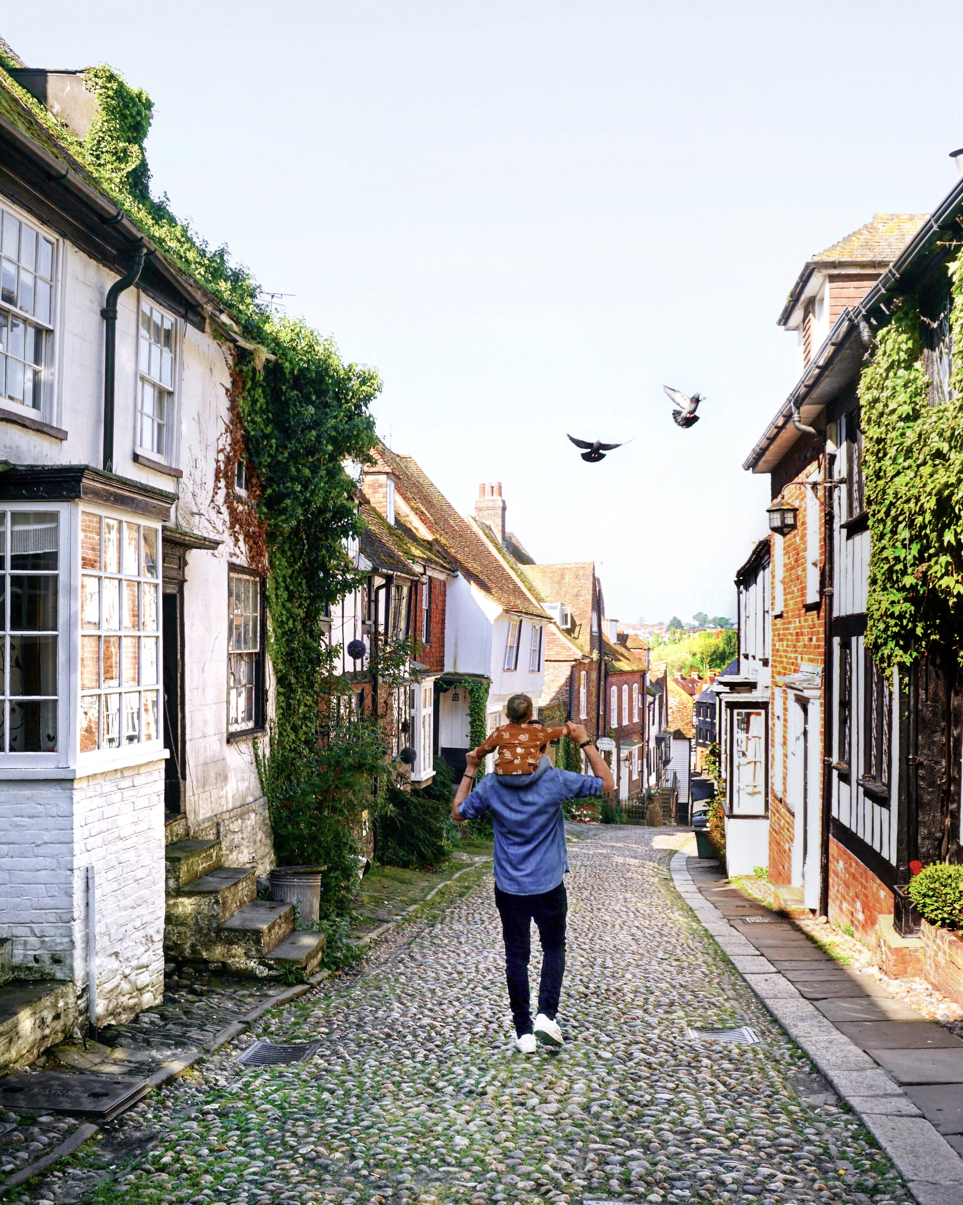 Man carrying child on his shoulders walking along street