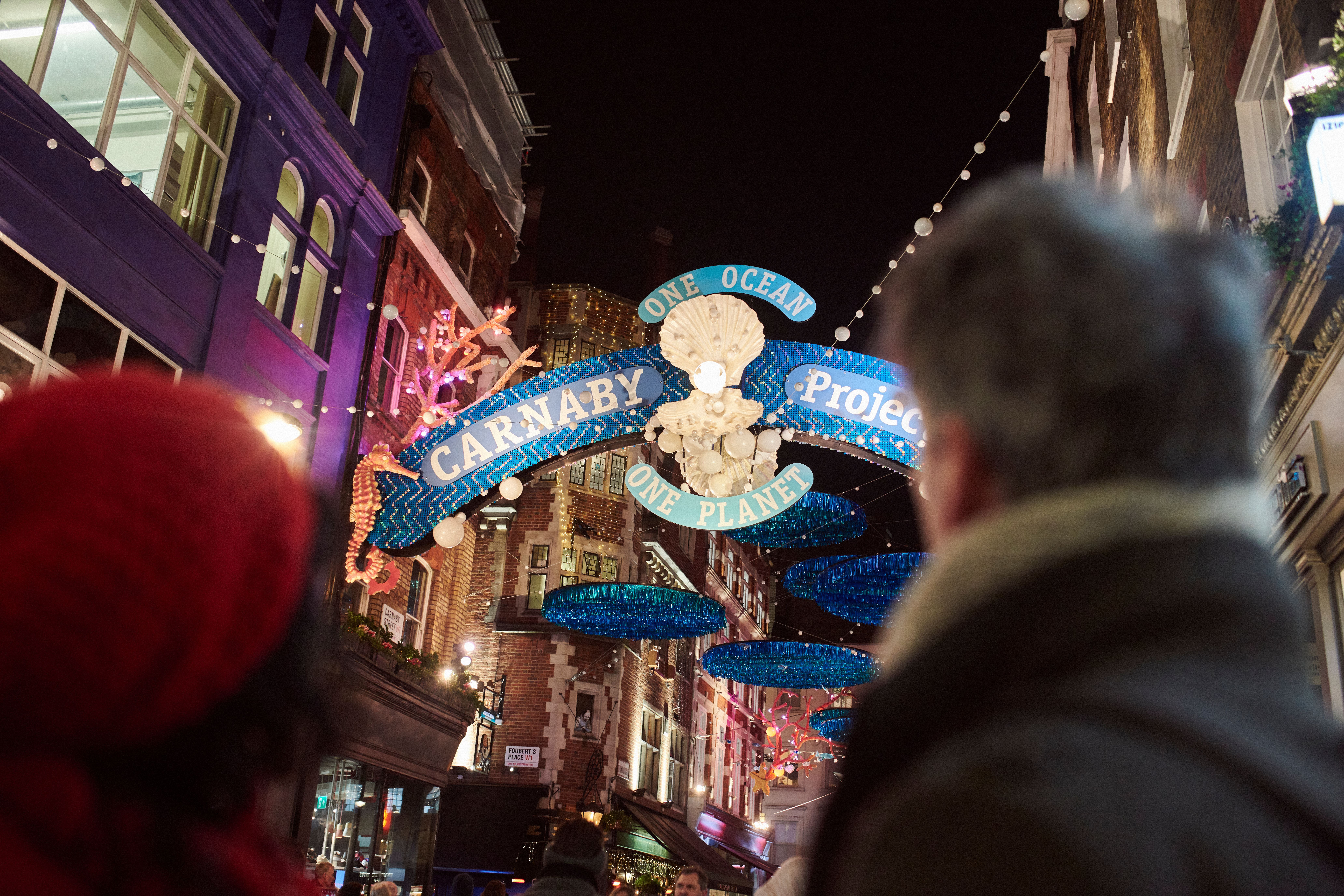 زوجان ينظران إلى أضواء الشوارع وزينة عيد الميلاد ولافتة شارع كبيرة