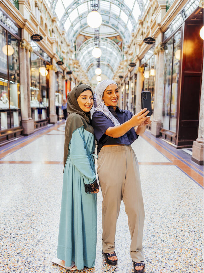 Two women take a picture together in an indoor shopping arcade