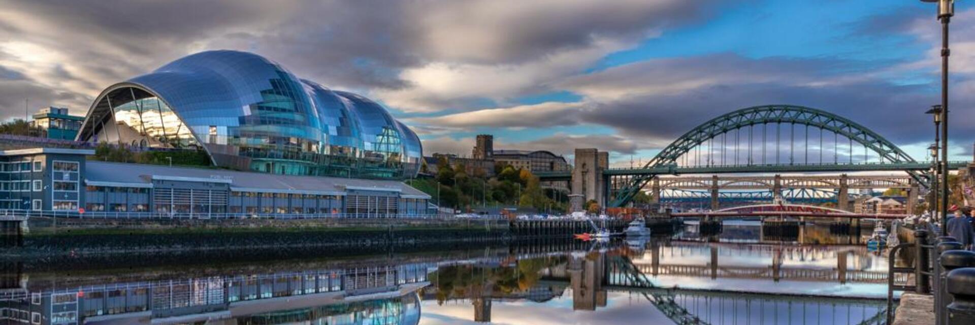 A modern glass international music centre along a calm river next to an arched bridge.