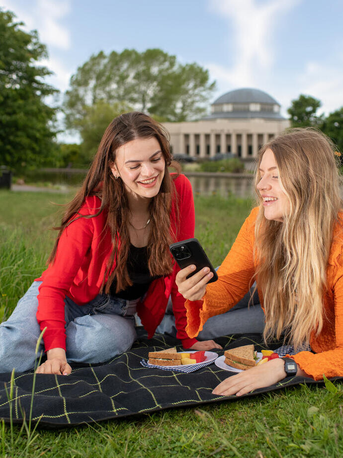 Two women sit on a blanket having a picnic