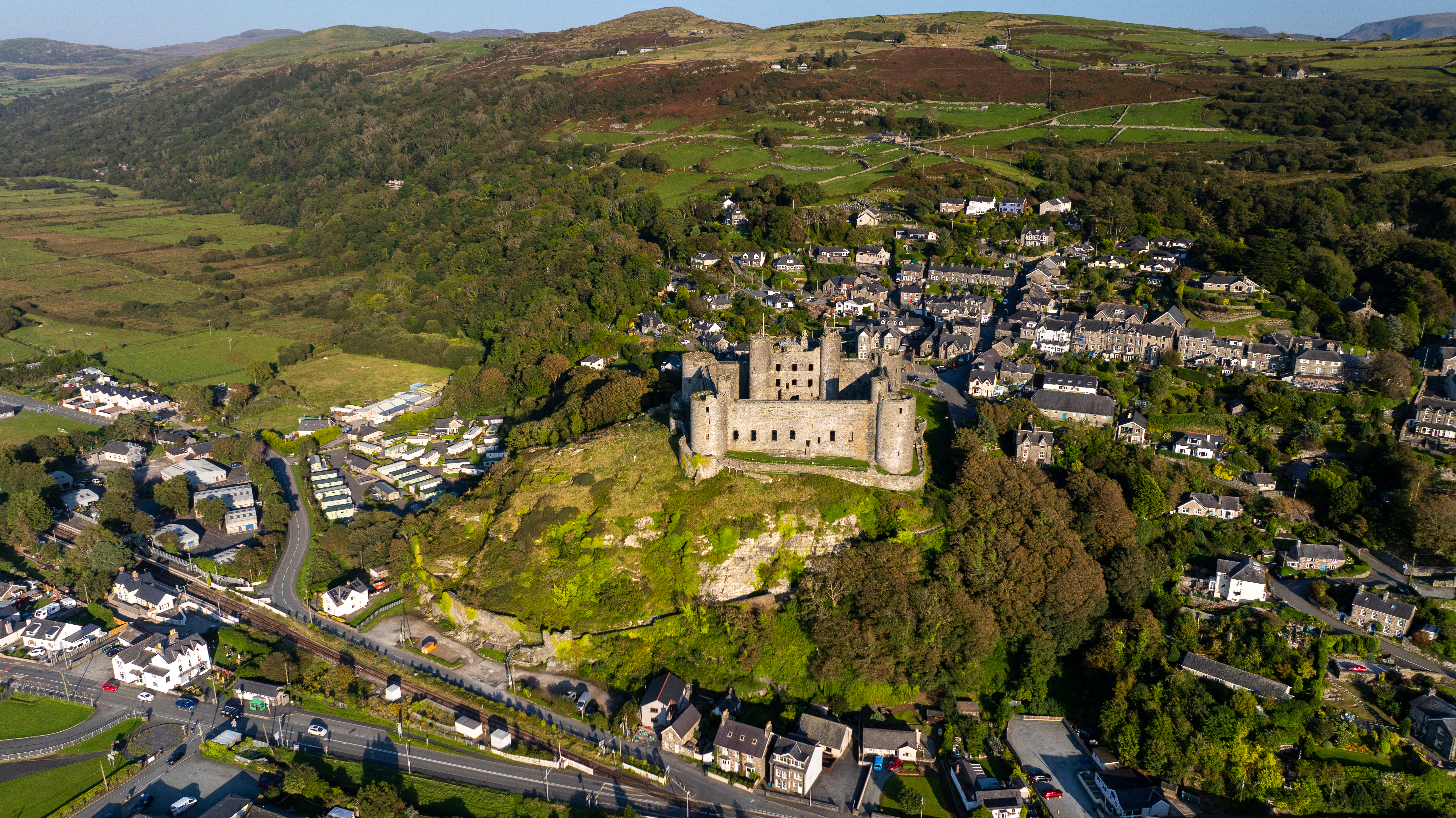 Aerial view of castle standing on a grassy hilltop surrounded by town and landscape