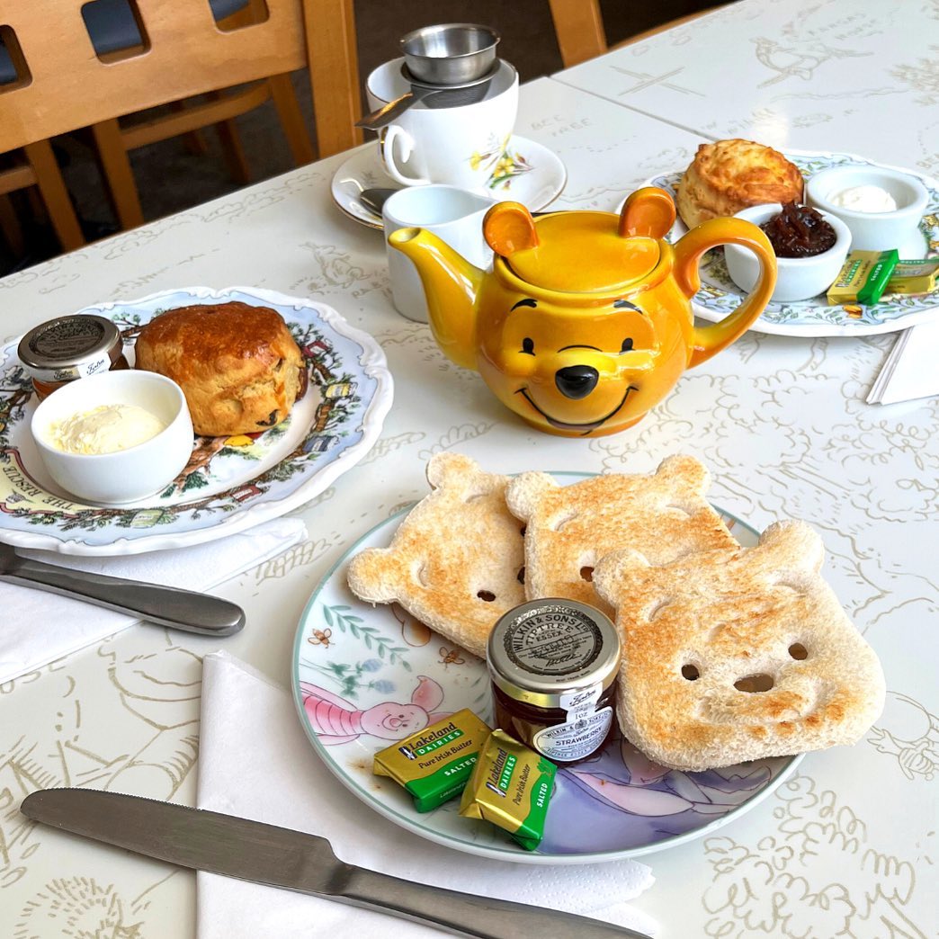 Afternoon tea setup with a Winnie the Pooh teapot, scones, bear-shaped toast, butter, jam, and tea cups on a decorated table.