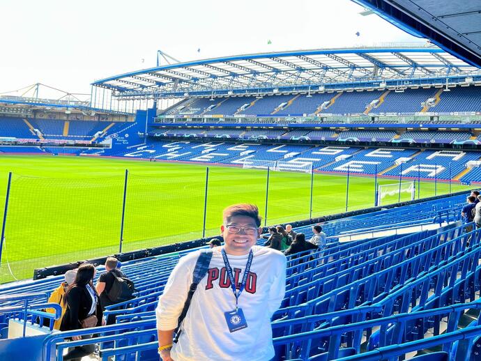 A person standing in front of the pitch on a stadium tour of Stamford Bridge, home of Chelsea Football Club