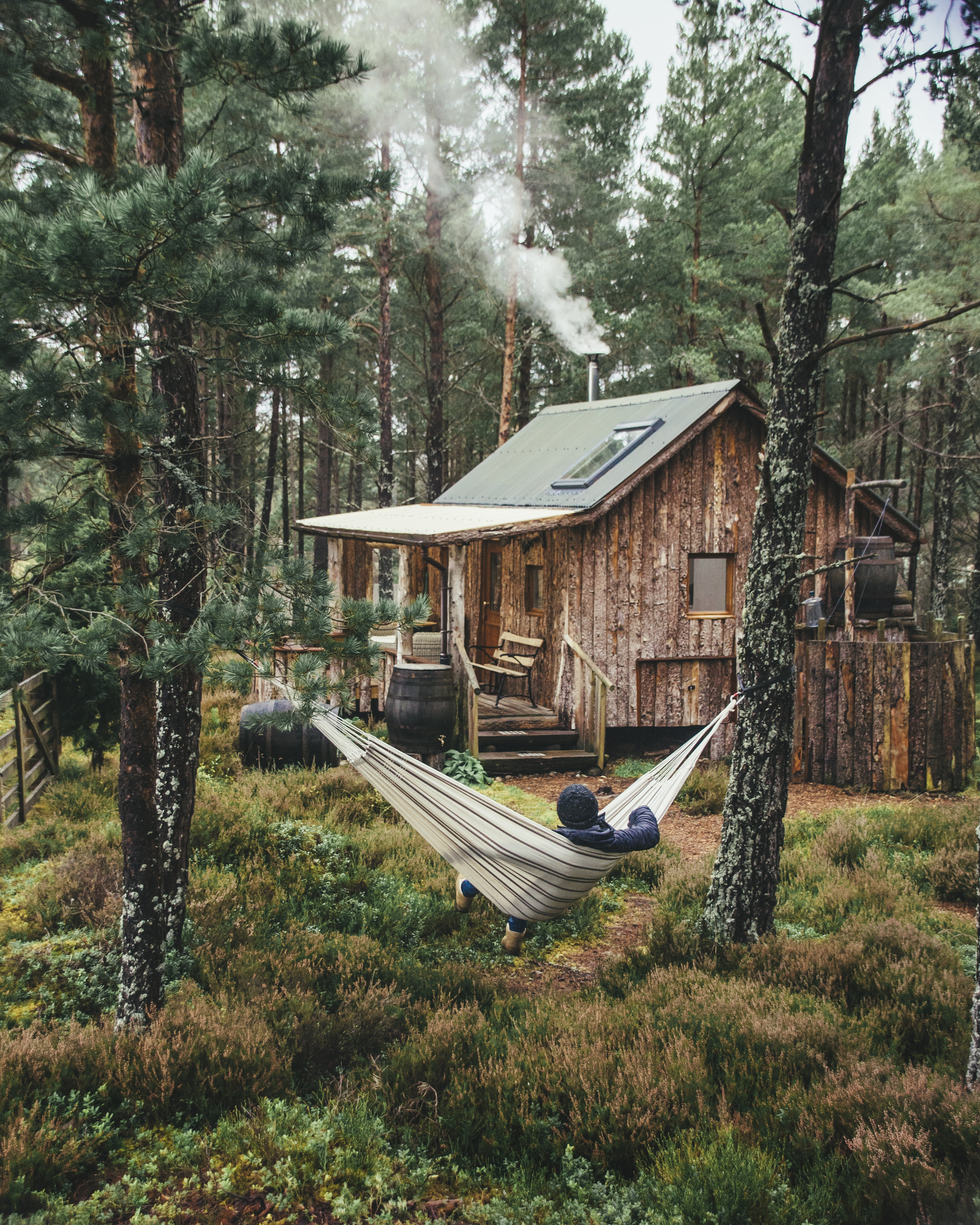 Man relaxing in a hammock outside a wooden cabin in a forest