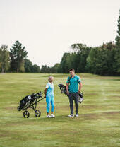 A man and a woman carrying golf clubs on a golf course