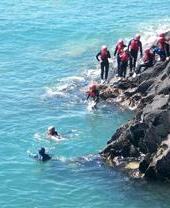 A group of people diving into the ocean off a rock coast in Cardiff, Wales