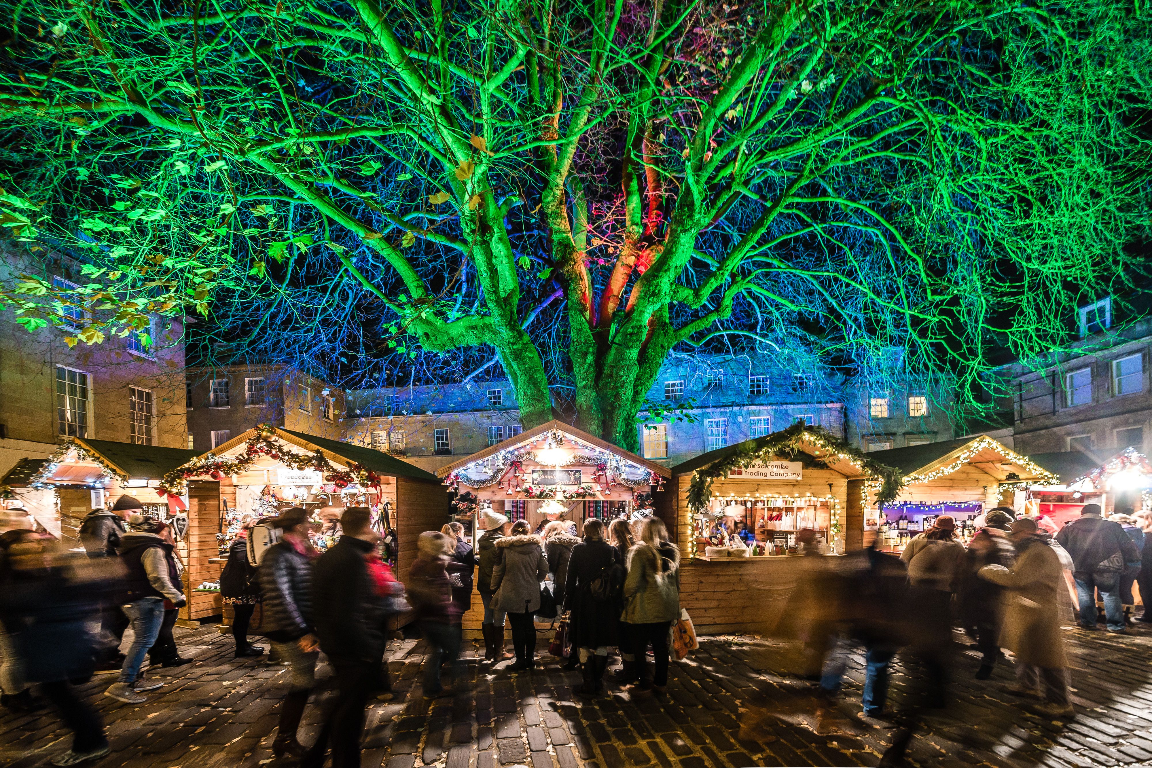 People visiting Christmas Market traders in wooden chalet huts in Bath