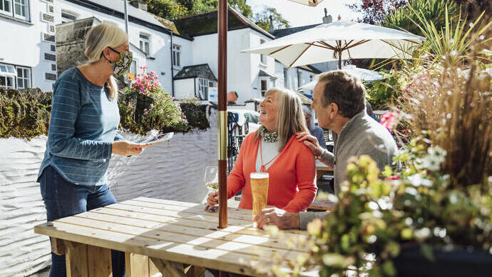 Couple sitting outside at a pub having a drink, talking to a member of staff