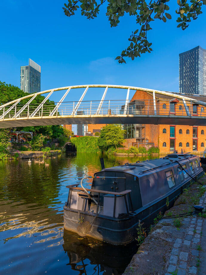 Bateau amarré sur un canal avec un pont piétonnier et des immeubles en arrière-plan