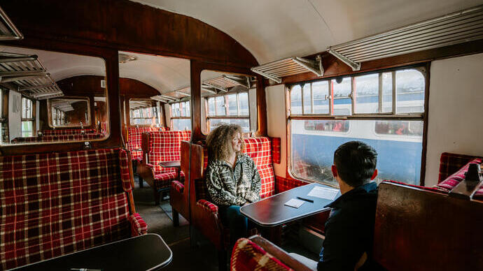 Un uomo e una donna seduti a un tavolo all'interno di uno scompartimento ferroviario.