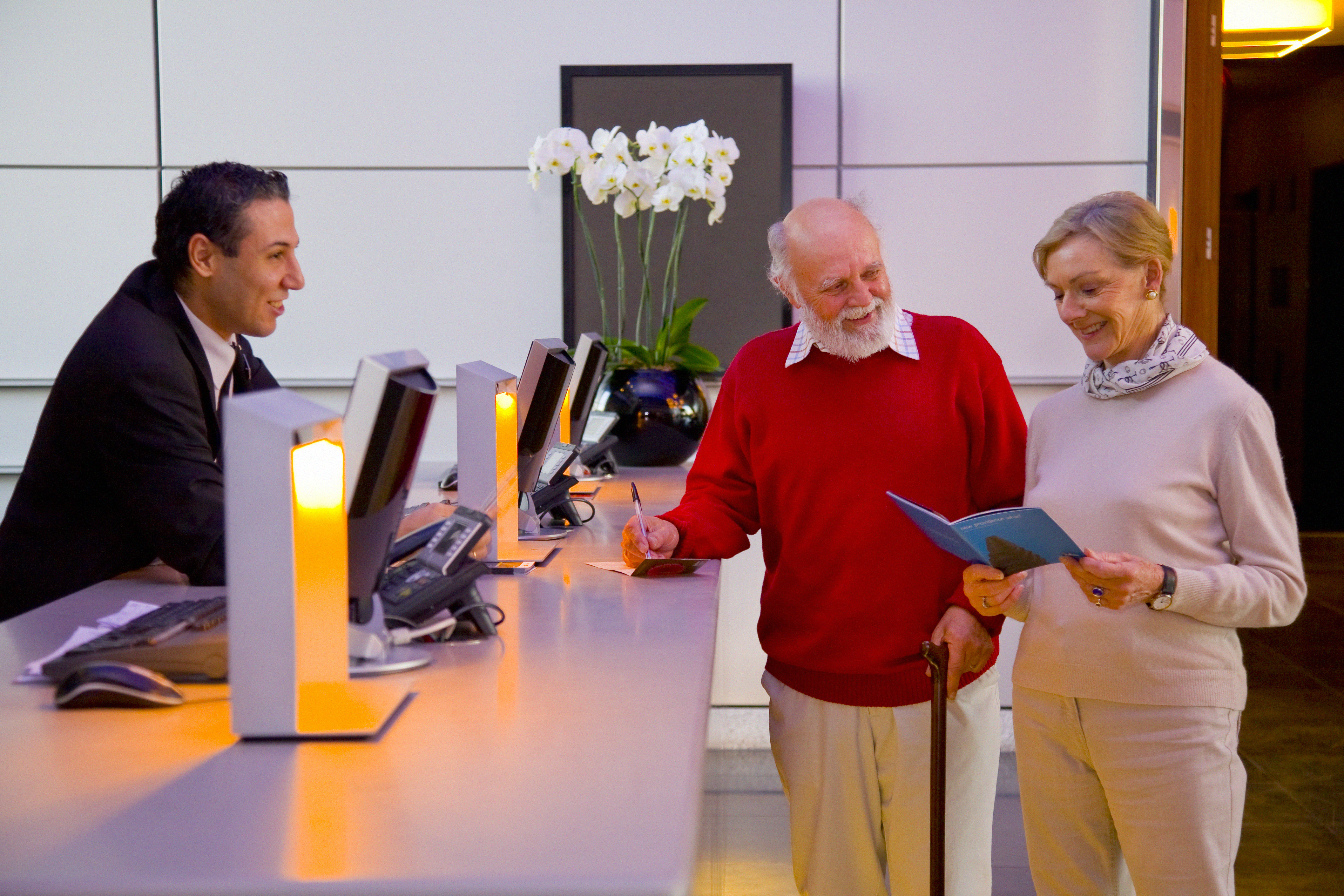 Couple, one with walking stick at a check-in desk of a hotel