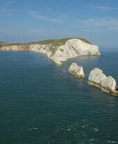 Alte colonne di gesso in fila che si estendono dalle scogliere della terraferma fino a un faro