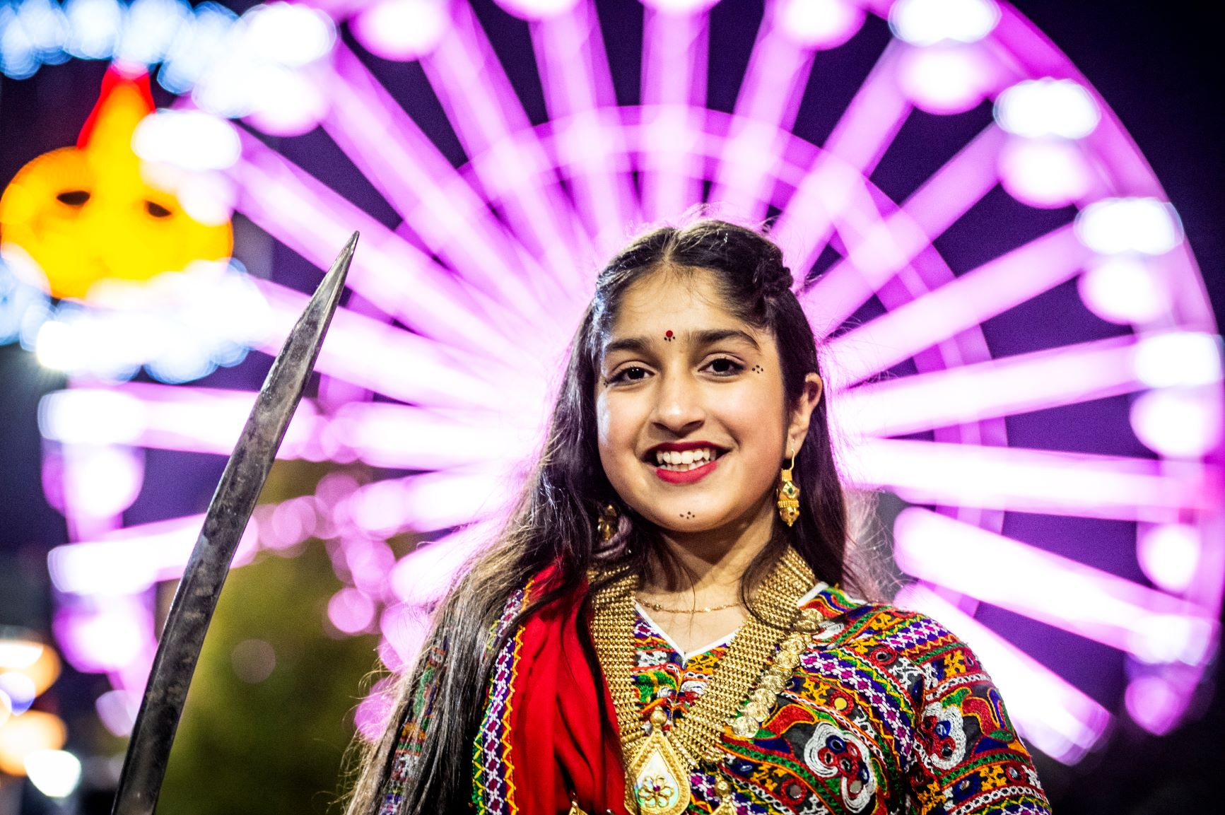 A woman celebrating Divali in front of a large lit up wheel