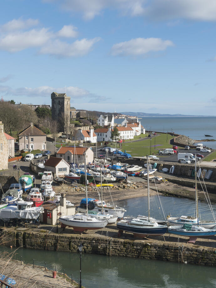 A small harbour with small sailing yachts and a few houses on a sunny day.