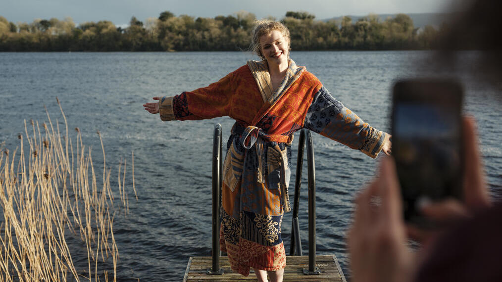 امرأة ترتدي رداء حمام تتألق أمام الكاميرا أمام بحيرة في إيليمنتس سبا تريل، فين لوغ