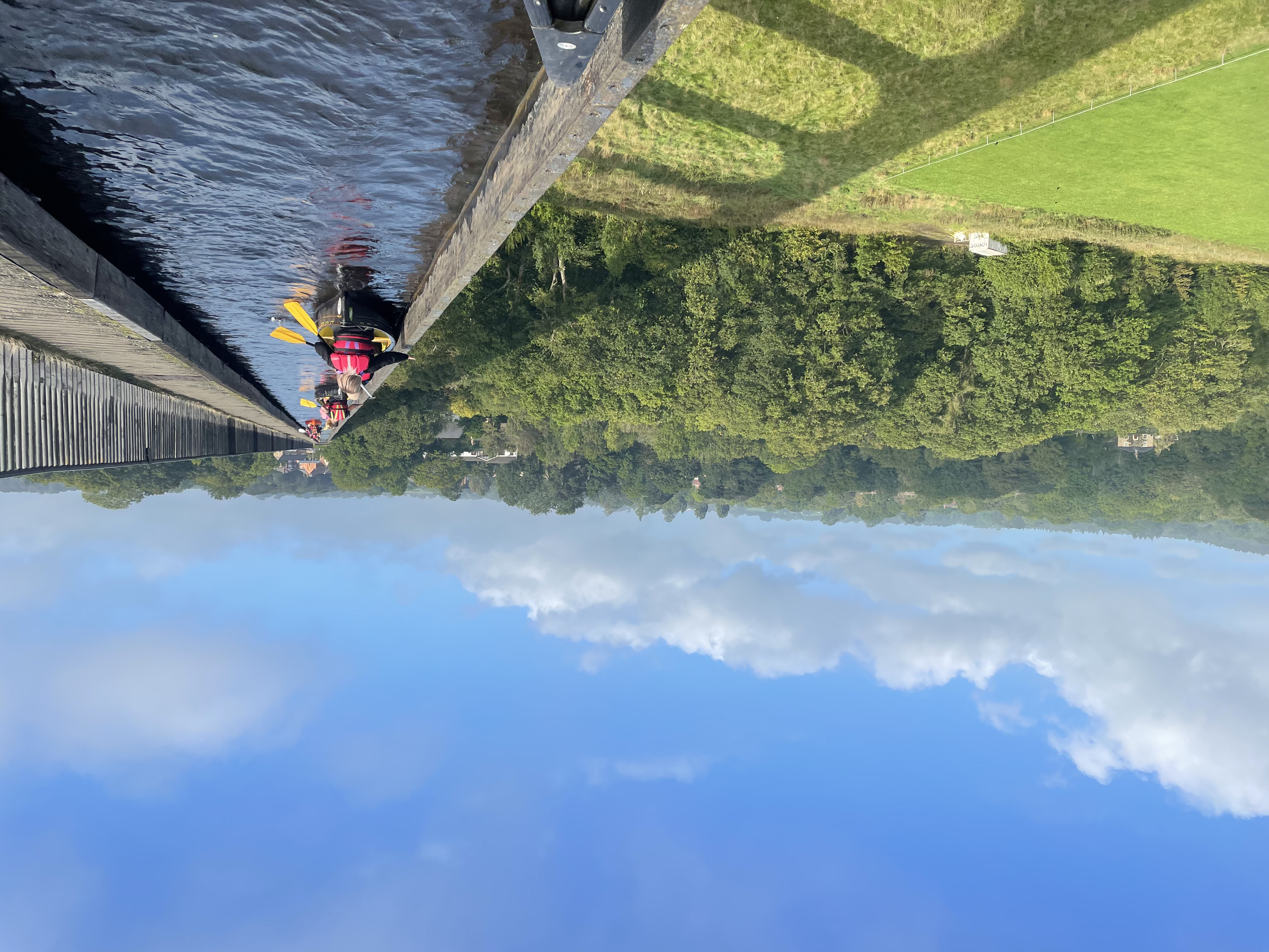 A group paddling kayaks across a viaduct with scenic views of Snowdonia/Eryri National Park